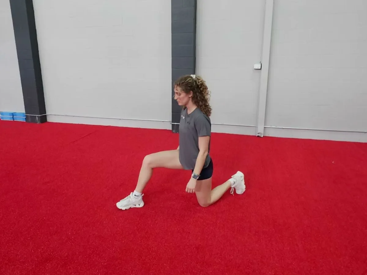 A member holding a half-kneeling hip flexor stretch on the turf