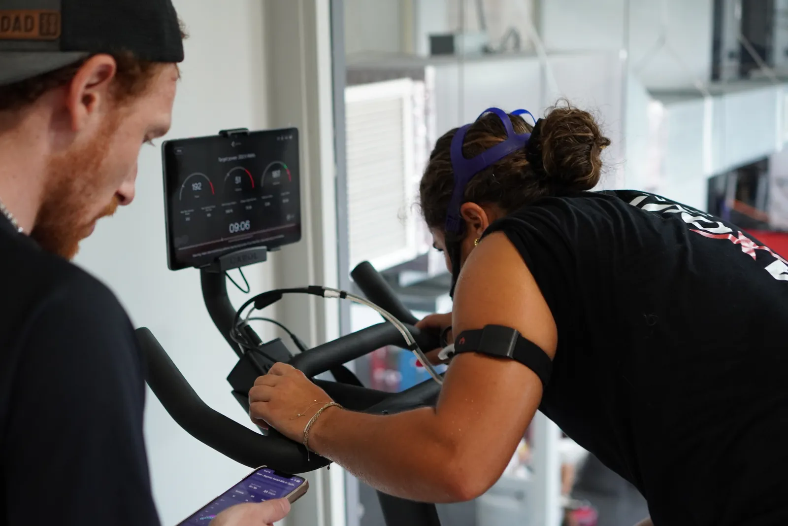 A coach reading live PNOĒ data while a member rides the bike