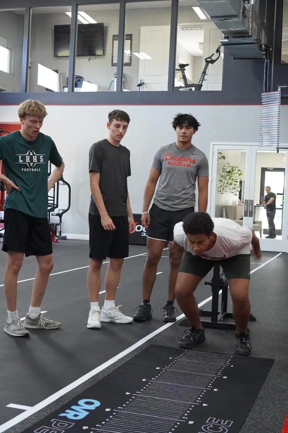 An athlete broad-jumping on the measured mat while teammates watch