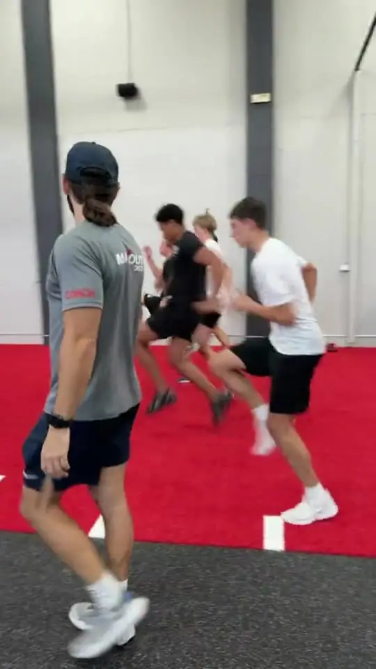 A coach running a group sprint drill on the red turf